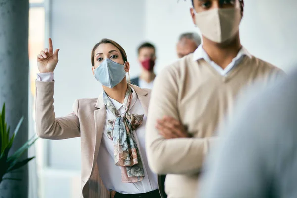 Impatient businesswoman trying to ask a question while waiting with in line with group of colleagues in a hallway during coronavirus pandemic.