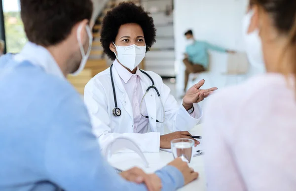 Black doctor wearing protective face mask while talking to her patients during an appointment at clinic.