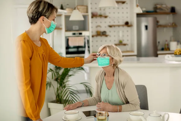 Mature woman getting help from her adult daughter in adjusting protective face mask during coronavirus pandemic.