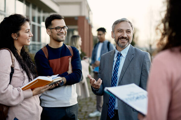 Happy university teacher and his students communicating outdoors after the lecture.