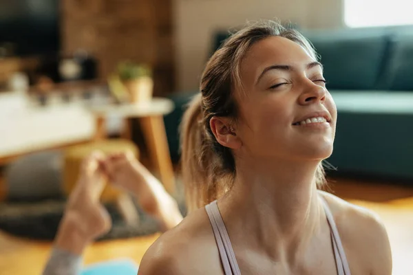 Close-up of smiling athletic woman doing relaxation exercises after sports training at home.