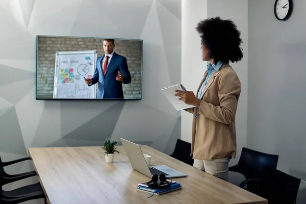 African American female entrepreneur following business presentation on projection screen from the office.