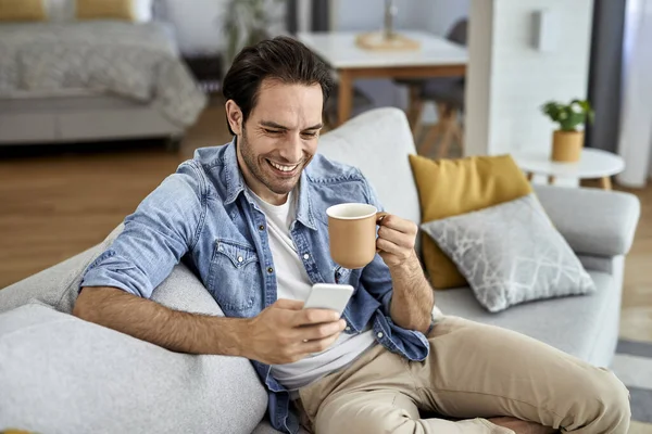 Young Happy Man Texting Smart Phone While Relaxing Sofa Drinking — 图库照片