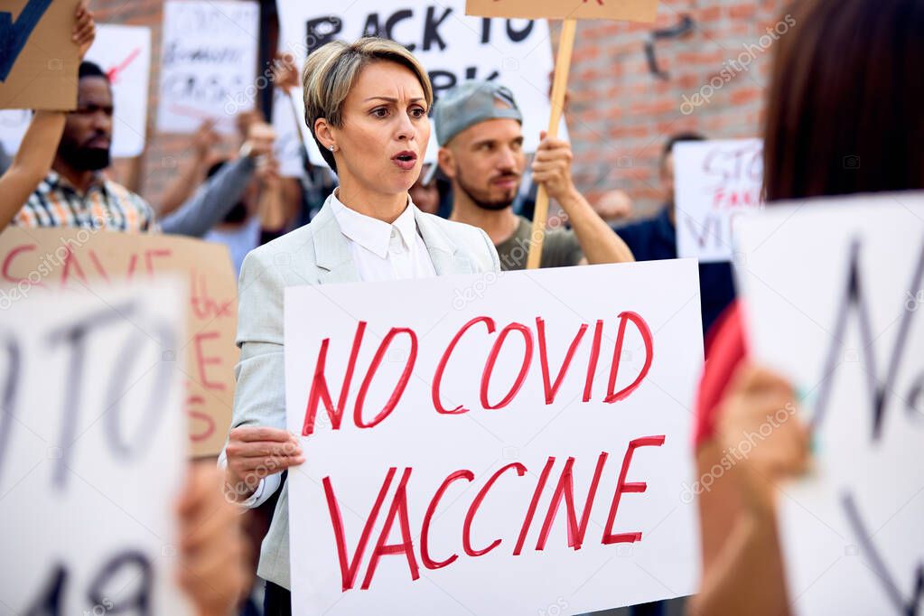Displeased woman holding 'no COVID vaccine' while supporting anti-vaccination movement and participating in a protest on city streets. 