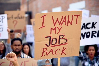 Crowd of unemployed people protesting after losing their jobs due to COVID-19 pandemic. Focus is on I want my job back sign. 