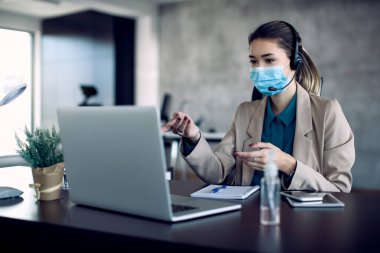 Businesswoman with face mask making video call over laptop while working in the office.