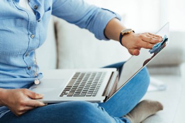 Unrecognizable woman cleaning her laptop with fabric cloth at home. 