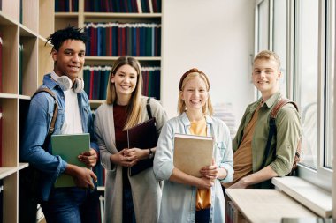 Multi-ethnic group of college friends standing in a library and looking at camera. 