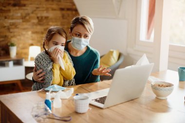 Worried mother talking to a doctor via video call while her daughter is feeling ill during coronavirus pandemic. 