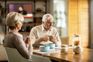 Mature man drinking coffee and reading newspaper while having breakfast with his wife at home. 