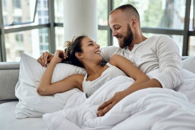 Happy couple in love resting on a bed and talking to each other in the morning. 