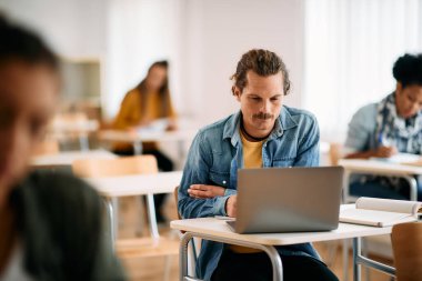 Male student learning on laptop while having lecture in the classroom.