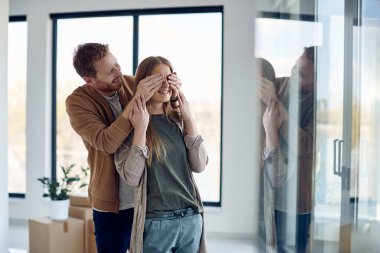 Happy couple having fun while buying their first home. Man is surprising his wife and covering her eyes. 