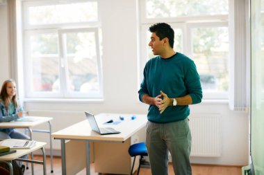 Male teacher talking to high school students while using smartboard during a class in the classroom. 