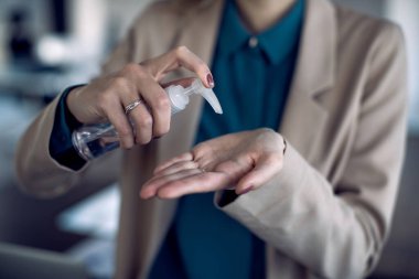 Close-up of businesswoman using hand sanitizer in the office during COVID-19 pandemic. 