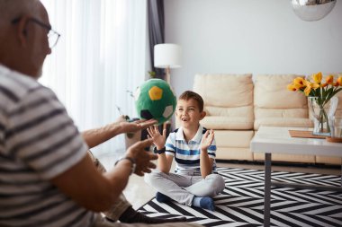 Happy boy having fun with his grandfather while playing with a ball at home. 