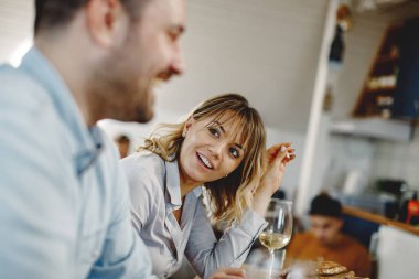 Smiling woman having a lunch with her husband and talking to him at dining table.