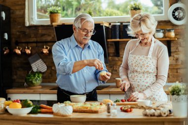 Happy mature couple preparing food together in their kitchen. 