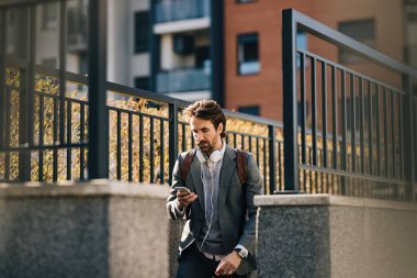 Young businessman using mobile phone and reading text message while walking outdoors. 