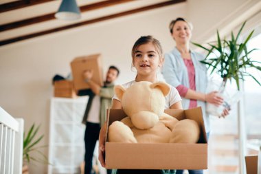 Little girl carrying her teddy bear while moving into new house with her parents. 