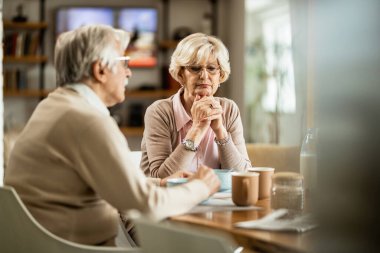 Mature couple thinking of something during breakfast time at home. Focus is on pensive woman. 