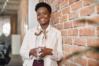 Satisfied African American businesswoman standing at corporate office and looking at camera.
