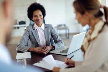 Happy African American insurance agent closing a deal her clients while the woman is signing a contract during the meeting. 