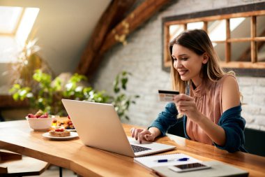 Happy woman using credit card and laptop while shopping on the internet at home. 