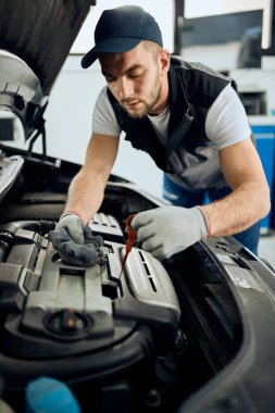 Young car repairman checking oil level during engine maintenance in a workshop.