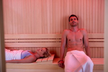 Smiling couple enjoying with eyes closed in sauna at health spa.