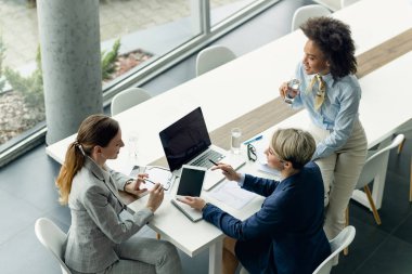 High angle view of happy businesswomen using touchpad and talking while working in the office. 