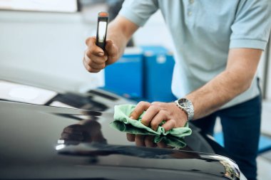 Araba tamircisinin yakın plan görüntüsü. Araç kaputunu lambayla inceliyor..