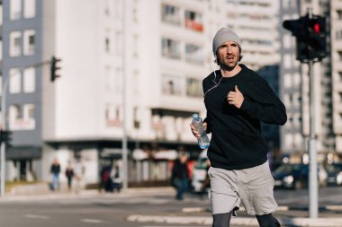 Young runner carrying bottle of water while jogging on the street. 