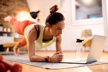 Athletic woman having online exercise class while using laptop at home. 