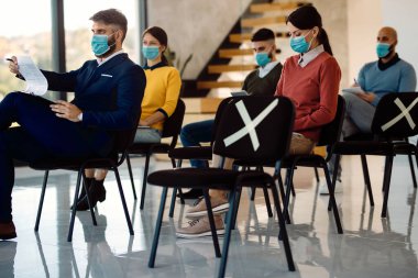 Group of entrepreneurs sitting on safe distance and wearing face masks while attending a seminar during COVID-19 pandemic.