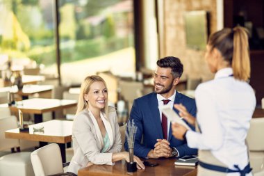 Happy business colleagues making an order and communicating with a waitress in a cafe. 