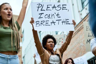 Low angle view of a black woman holding banner with I can't breathe inscription while demonstrating for human rights with crowd of people. 