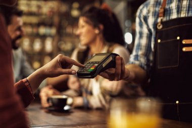 Close-up of woman entering pin at credit card reader while paying bill in a pub. 