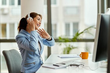 Happy businesswoman working on a computer and having fun while listening music over headphones. 