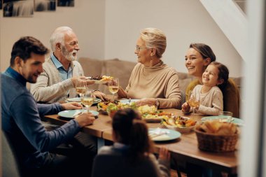 Happy extended family having a meal together in dining room. Focus is on mature couple passing food to each other. 
