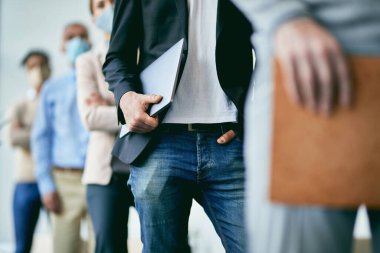 Unrecognizable male entrepreneur holding his laptop while standing in a row with group of colleagues in a lobby due to COVID-19 pandemic. 