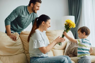 Happy mother receiving bouquet of yellow flowers from her son at home. 