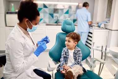 African American female dentist communicating with a boy before teeth check-up at dental clinic.