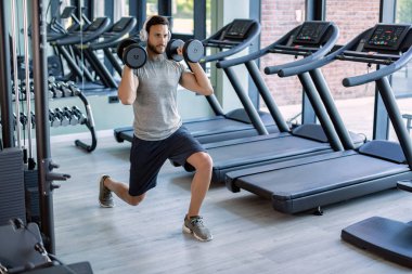Young athletic man having weight training in lunge position in a gym. 