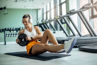 Smiling sportswoman doing abdominal exercise with weight plate at health club. 