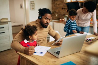 Multi-tasking African American man working while being with his family at home. 