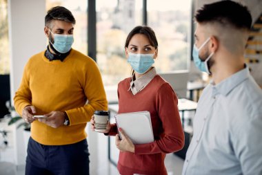 Group of entrepreneurs with protective face masks communicating while working in the office. Focus is on woman. 