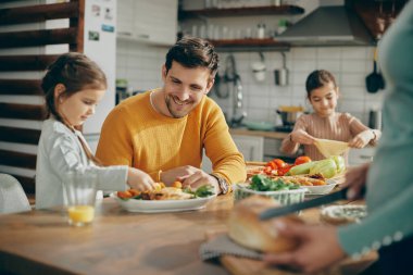 Happy family preparing dining table for lunch at home. Focus is on father. 