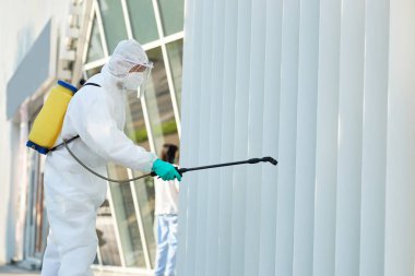 Disinfectant worker in protective suit sanitizing city area in order to prevent spread of COVID-19.