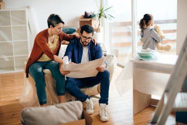 Couple talking while examining housing plans and moving into a new home with their daughter. 
